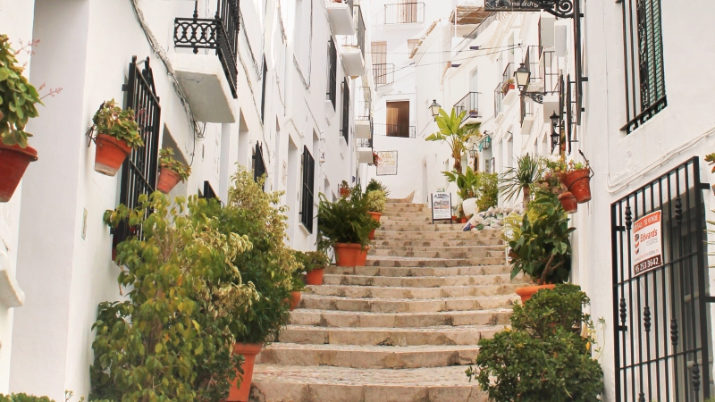 Manga trappsteg med blomsterkrukor mellan vita stenfasaded i Almunecar