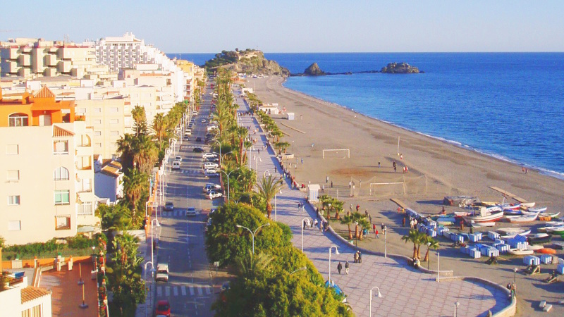Flygbild over strandpromenad, strand och gata langs havet